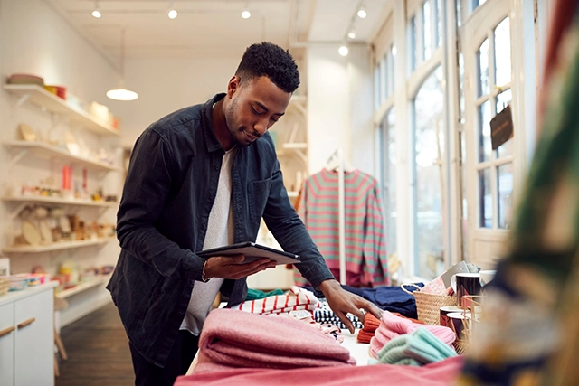 A customer thoughtfully assessing clothing items in a retail shop, representing the enduring value of in-person shopping experiences alongside e-commerce trends.