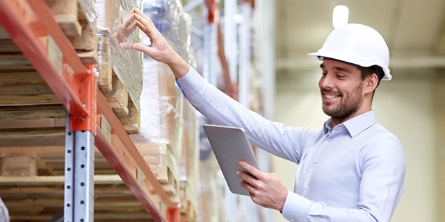 A smiling warehouse worker with a hard hat using a tablet to manage inventory, exemplifying efficient fulfillment operations